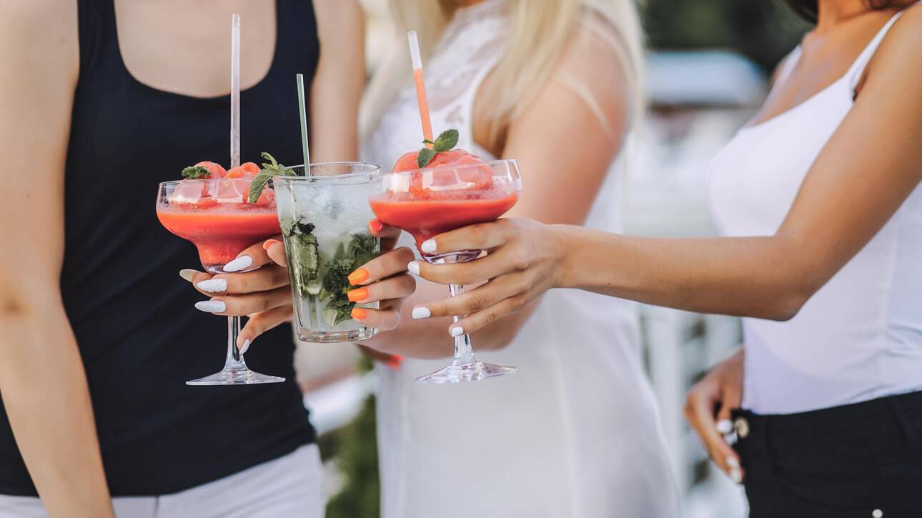 three young beautiful and stylish girls are standing by the water and drinking cocktails